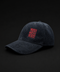 A dark washed corduroy baseball cap with a red embroidered square patch on the front that reads 'LIVE MORE MIGHT LESS' in a layered, shadowed design, set against a solid black background.