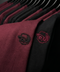 Close-up of a row of crewneck sweatshirts on black hangers, showing a heathered burgundy/maroon version with a black embroidered skull wearing a hat, and a black version with a red embroidered skull wearing a hat.