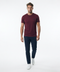 A man wearing a short-sleeve crewneck t-shirt in maroon, paired with dark navy pants and white sneakers, walking forward against a solid white studio background.