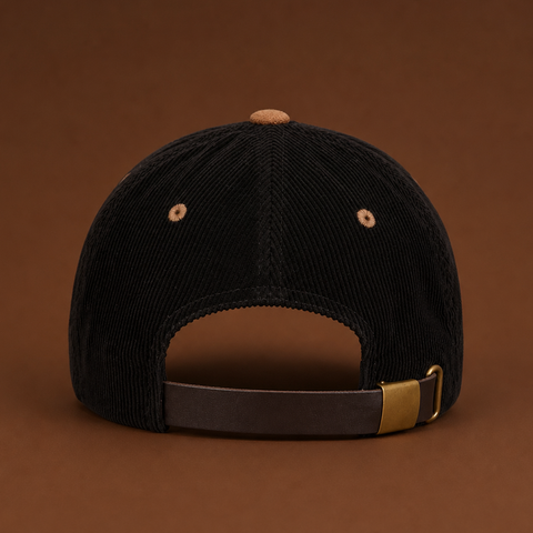 Rear view of a black corduroy baseball cap with a brown adjustable strap and a gold-tone metal buckle, set against a solid brown background.