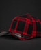 A structured baseball cap featuring a red and black plaid pattern, photographed on a dark studio background. The cap has a curved brim with a light gray underside and a visible New Era 9FIFTY sticker on the front.