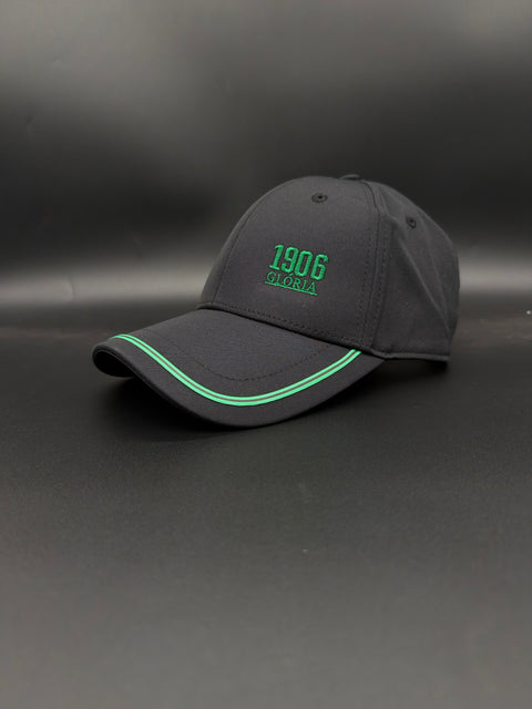 A dark gray baseball cap with green embroidered text reading '1906 gloria' on the front, displayed on a dark gray background.