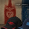 Two baseball caps for Benfica are displayed on a wooden surface against a textured background featuring the club's red and blue colors. The cap in the foreground is black with red embroidery and a red piping accent on the brim, while the cap behind it is navy blue with light blue embroidery and a light blue piping accent.