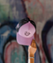 A pink and black trucker cap with a cartoon graphic on the front, held up by a hand against a blurred graffiti wall background.
