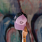 A pink and black trucker cap with a cartoon graphic on the front, held up by a hand against a blurred graffiti wall background.