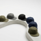 Six flat-brim baseball caps in olive green, charcoal gray, black, navy blue, and khaki green, arranged on a curved white display riser against a clean white background.