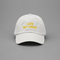A white cotton baseball cap with yellow embroidered text reading 'LATE BUT GREAT' on the front, photographed against a solid gray background.