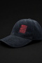 A dark washed corduroy baseball cap with a red embroidered square patch on the front that reads 'LIVE MORE MIGHT LESS' in a layered, shadowed design, set against a solid black background.