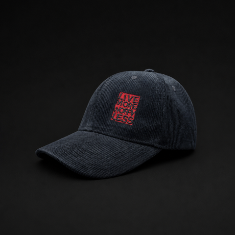 A dark washed corduroy baseball cap with a red embroidered square patch on the front that reads 'LIVE MORE MIGHT LESS' in a layered, shadowed design, set against a solid black background.