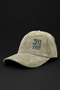 A light olive green corduroy baseball cap with a black embroidered square patch on the front that reads 'LIVE MORE WORRY LESS'. The cap is photographed on a solid black background.
