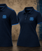 Two navy blue polo shirts displayed side by side against a textured brown and blue background. Both shirts feature light blue trim on the collar and sleeve cuffs, with a light blue embroidered '1899 A.