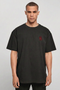 A man wearing an oversized black t-shirt with a small red embroidered skull graphic on the left chest, photographed against a neutral light gray background.