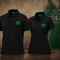 Two black short-sleeve polo shirts with green trim and '1906 GLAMORA' printed on the chest, displayed side by side against a textured brown wall with a green Sporting Portugal crest.
