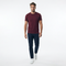 A man wearing a short-sleeve crewneck t-shirt in maroon, paired with dark navy pants and white sneakers, walking forward against a solid white studio background.